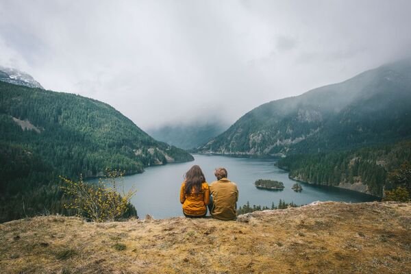Two people walking on a path near a lake with mountains in the background